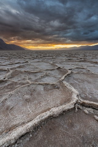 Sunset in Badwater basin with dark clouds in the sky with golden hues in distance